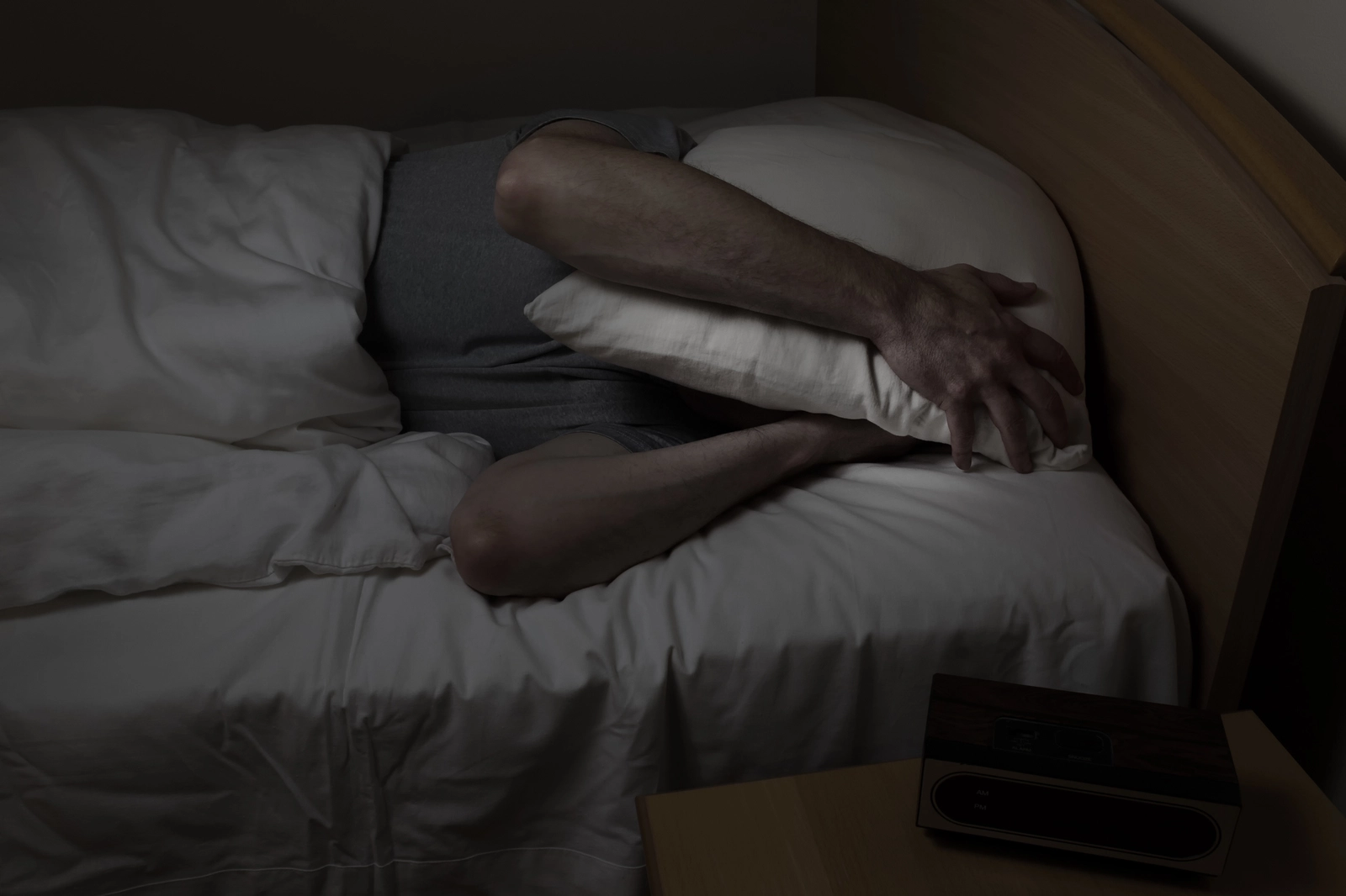 Ambien Withdrawal Symptoms: A person in a dark room in bed, holding a pillow over their head.