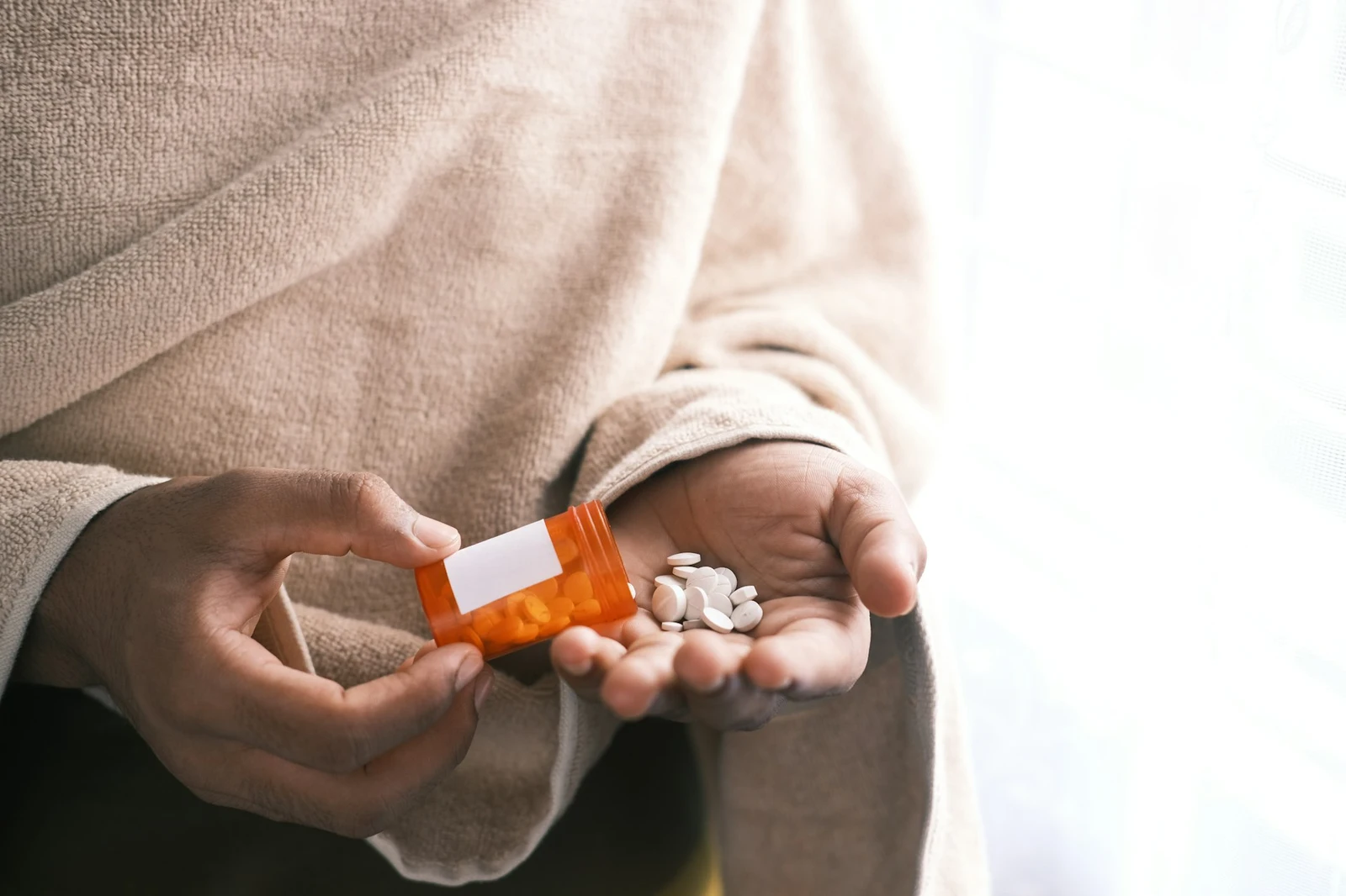 Are Muscle Relaxers Addictive? A person pouring white pills into their hand from a prescription pill bottle.