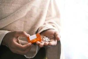 Someone taking pills from a pill bottle and possibly wondering about the half life of gabapentin.
